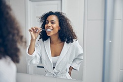 woman brushing her teeth in front of a mirror